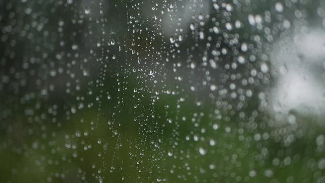 Strong rain water flushes against window glass and streaming down. Close-up. Raindrops on glass background in rainy season