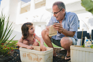 grandfather and granddaughter plant seeds in backyard garden