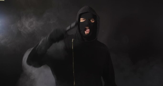 Robber in black clothes, mask and gloves with a gun talking aggressive to camera on black studio background with smoke. Security system concept.  4K 50 fps slow motion