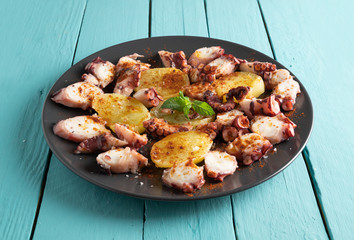 cooked octopus presented sliced with potatoes, blue wood background