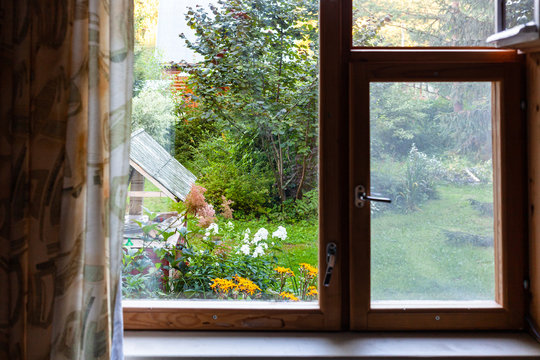 View Of Ornamental Garden With Well Through Window In Country House In Summer Twilight