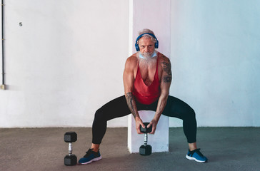 Fototapeta na wymiar Senior man doing gym workout with dumbbells while wearing face protective mask during Coronavirus isolation quarantine - Fitness, sport and healthy elderly lifestyle - Focus on face