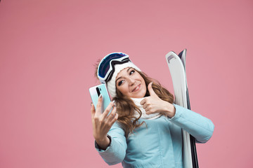 fun skier takes a selfie on her smartphone. A young woman with ski equipment in a jacket and hat,