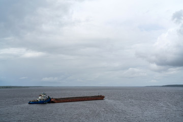 The barge floats down the river on a cloudy day. Transportation of goods by water.