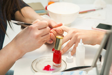 Gel polish design. Female master in the salon is painting with brush on the hands of the client. Beauty industry, creativity concept