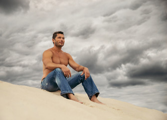Fototapeta na wymiar Pensive handsome young man sitting on the dunes in desert