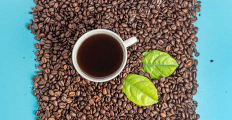White cup with freshly brewed aromatic coffee and coffee beans stacked in a rectangle on a blue background