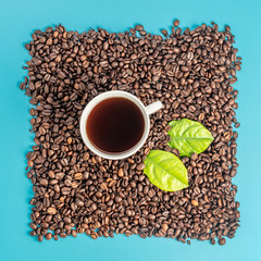 White cup with freshly brewed aromatic coffee and coffee beans stacked in a rectangle on a blue background