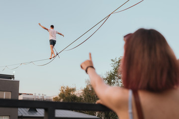 Male athlete demonstrates his skills by balancing on a narrow slackline stretched between two...