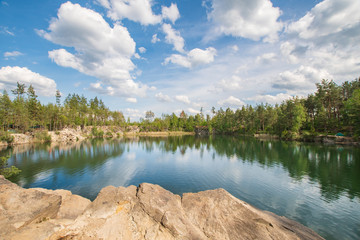 Fototapeta na wymiar High Stone career and it's lake in forest surrounded by rocks summer landscape
