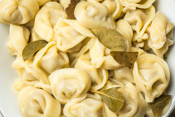 Handmade boiled shaped dumplings with bay leaves in large plate on kitchen table.