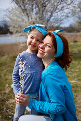 little girl child and mother woman walks through the spring forest with flowering trees, laugh and play, the beginning of spring, family vacation, love of parents