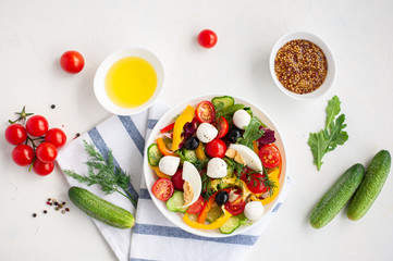 Salad of multi-colored vegetables with mozzarella and egg and ingredients from which it is made on a white concrete background.