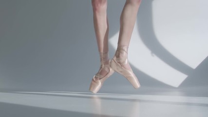 Young ballerina dancing ballet on the tiptoes, feet in pointe tied with ribbons closeup on white background. Slow motion.