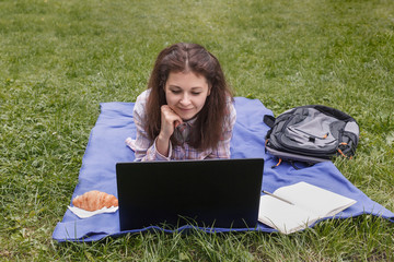 Workplace on a blue rug in nature. Woman lying on her stomach near laptop and have online learning,...