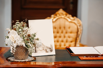 A wedding guestbook setup with a bouquet and artistic illustrations on a vintage desk.