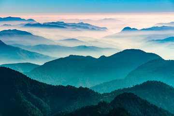 View of Himalayas mountain range with visible silhouettes through the colorful fog from Khalia top trek trail. Khalia top in himalayan region of Kumaon, Uttarakhand, India. - obrazy, fototapety, plakaty
