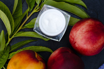 Peaches, a peach twig close-up and a jar of cream on a black slate board. Beauty concept. View from above