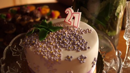 21 Birthday Cake on table. Purple decor flowers. White candles number twenty one not burning. Isolated.
