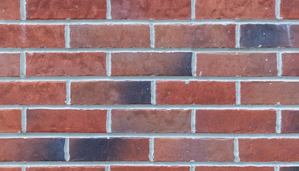 Vintage stained brick wall colored in red, orange, black with paint splatter on it's surface and white seams, background texture for interior and exterior design, wide banner