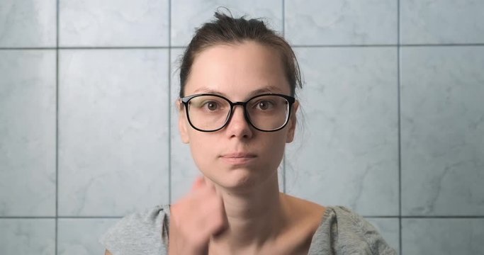 Portrait of woman in glasses pretending shaving her beard in bathroom, front view. She is looking at camera and smiling. Joke, funny video in slow motion.