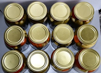 Home canning. Top view of glass jars with salted or pickled cucumbers and tomatoes. The jars are covered with yellow metal covers.