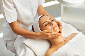 Fototapeta na wymiar Spa facial massage. Beautician makes face massage to woman in white beauty salon