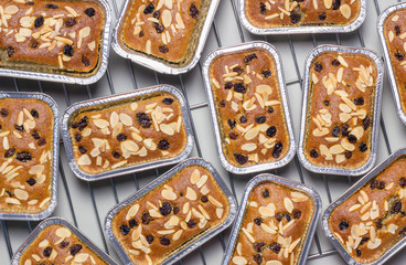 Image of banana cake in square containers sprinkled with almonds and raisins or bread, flat lay view. several pieces on a wire rack is desserts and sweet food.
