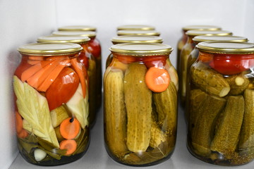 Home canning. Glass jars with salted or pickled cucumbers, tomatoes, carrots and zucchini. Spices and spicy herbs are laid at the bottom of the jar. The jars are covered with yellow metal covers.