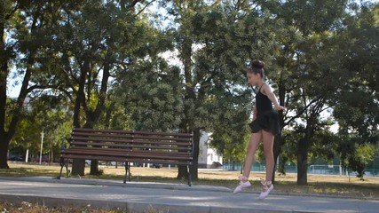 Beautiful Caucasian girl of eight years in black  ballet suit dancing ballet  in a city park on a sunny summer day.  Slow motion 200 fps 