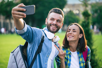 Beautiful young happy couple in casual clothes with backpacks are making selfie photo on smartphone