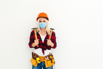 Builder girl in respiratory mask in denim overalls and a cap posing on a white background