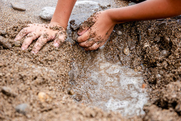 child plays on the beach in the sand. Children's hands in the sand on the beach close-up. A child builds a sand castle. On the seashore. On the ocean. Dirty sand by the sea