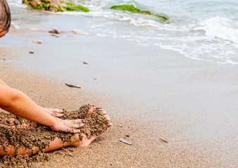 child plays on the beach in the sand. Baby hands and feet in the sand on the beach close-up. A child builds a sand castle. A child on the seashore. By the ocean. Dirty sand by the sea