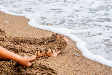 child plays on the beach in the sand. Baby hands and feet in the sand on the beach close-up. A child builds a sand castle. A child on the seashore. By the ocean. Dirty sand by the sea