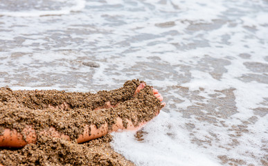 child plays on the beach in the sand. Baby hands and feet in the sand on the beach close-up. A child builds a sand castle. A child on the seashore. By the ocean. Dirty sand by the sea