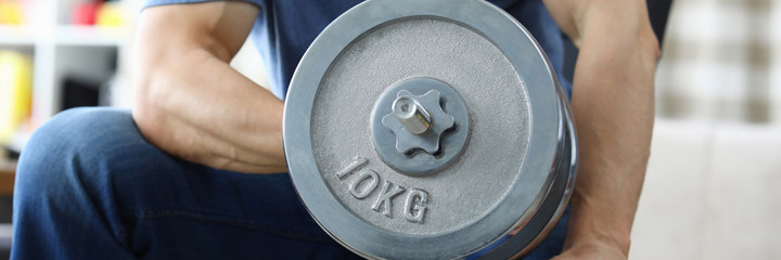 Close-up of strong male person exercise at home with heavy dumbbell. Training for fit and resilient body. Sport and active lifestyle. Indoors workout on quarantine concept