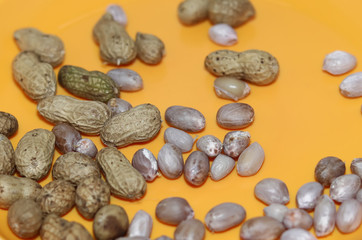 Peanuts in shells on yellow background. Raw peanuts top view isolated on yellow plate background