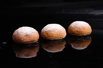 Baking on a black background. White buns sprinkled with powder and flour.