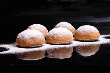 Baking on a black background. White buns sprinkled with powder and flour.