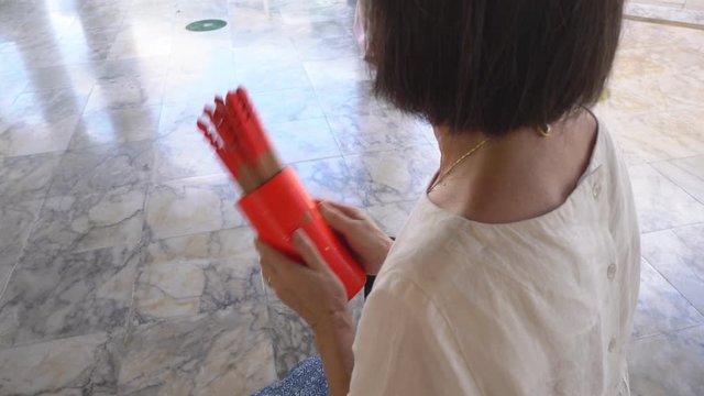 In temple, senior asian buddhist woman shaking Chinese Fortune Telling sticks or chi chi stick to forecast the future 