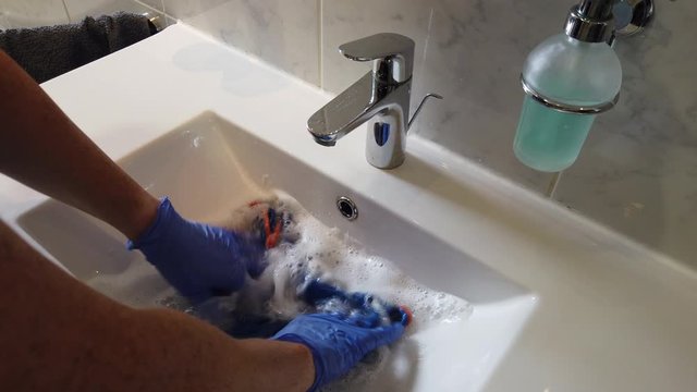 Hand mit Gummihandschuhen reinigt Bad Waschbecken Toilette WC