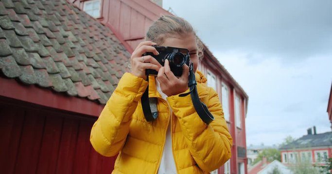 Young female tourist in scandinavian town makes photos on analog vintage camera. Shoots and captures memories of travel adventure experience in nordic city. Wanderlust concept or travel blogger