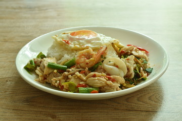 spicy fried seafood and meat chili and herb on rice topping egg in plate