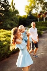 Naklejka na ściany i meble Adorable mom hold cute daughter in loving arms, smiling, hugging, lovely parents with little baby girl walking at the park, enjoy happy family moments, weekend outdoors concept