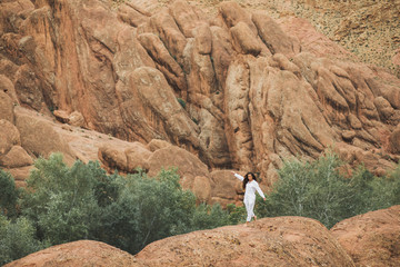 White woman walking on background of Todra gorge canyon landscape in Morocco. Red color mountains...
