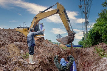 Asian workers inspect a massive sewer buried underground at a construction site. The excavator is...