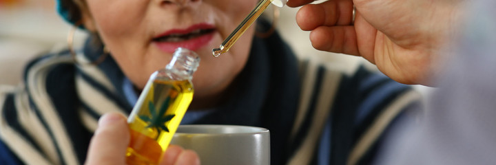 Close-up of elderly woman receives sedative drops from doctor. Glass bottle with leaf sign. Prescription herbal meds. Traditional medicine cannabinoid oil and healthcare concept