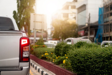 Luxury rear corner of pickup  silver car on the road. With Trees planted on the side of the road and the blur of the city. Open brake light.