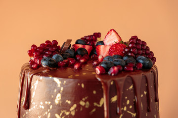 Appetizing chocolate cake decorated with strawberries, blueberries and a pomegranate on an orange background.